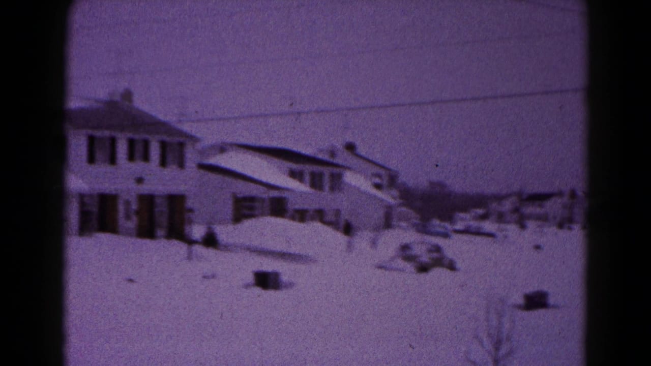 1959 Hagerstown home-movie frame showing a snow-covered suburban house, yard, and nearby street under a purple film cast.