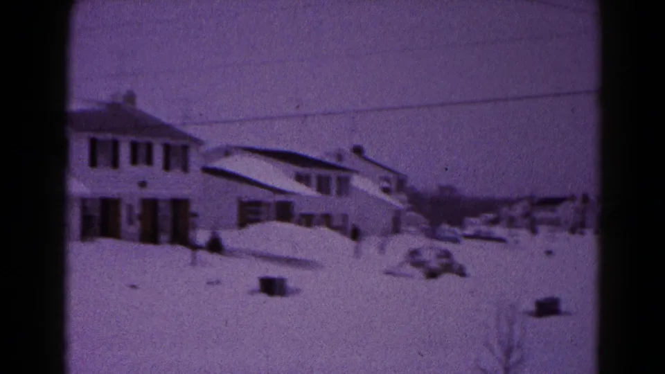 1959 Hagerstown home-movie frame showing a snow-covered suburban house, yard, and nearby street under a purple film cast.