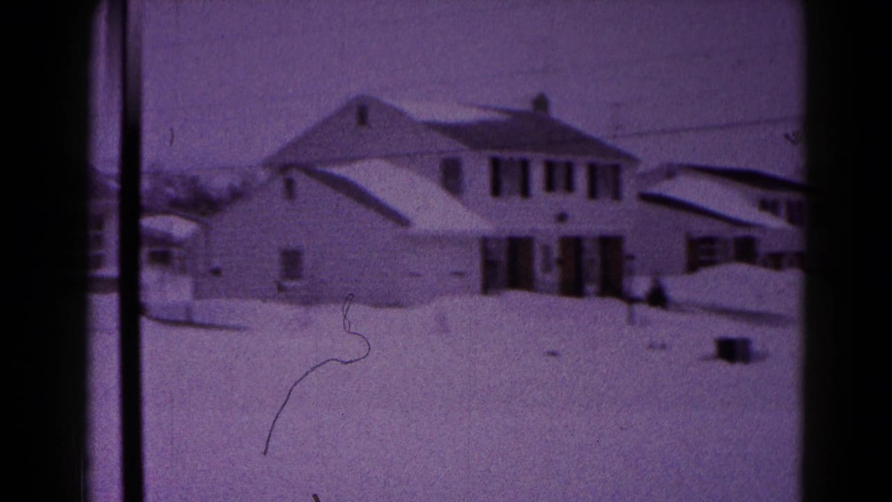 Suburban house with snow on the roof and yard, framed by dark film borders.
