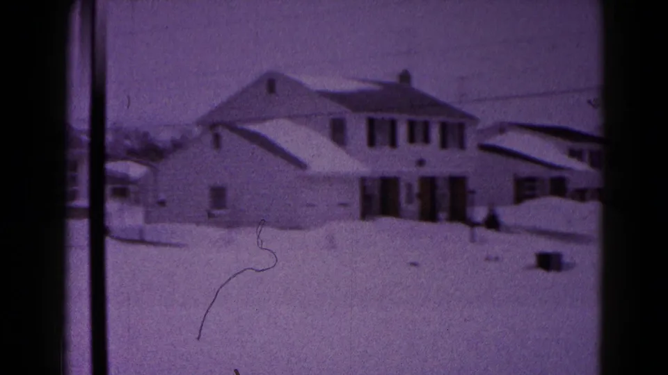Snow-covered Hagerstown residential exterior with dark shutters, roof snow, and open yard in a 1959 8mm frame.