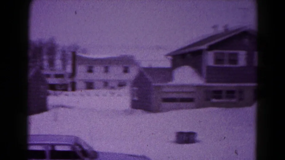 Hagerstown winter home-movie frame showing snow-covered houses, a partly visible parked car, and bare trees in 1959.