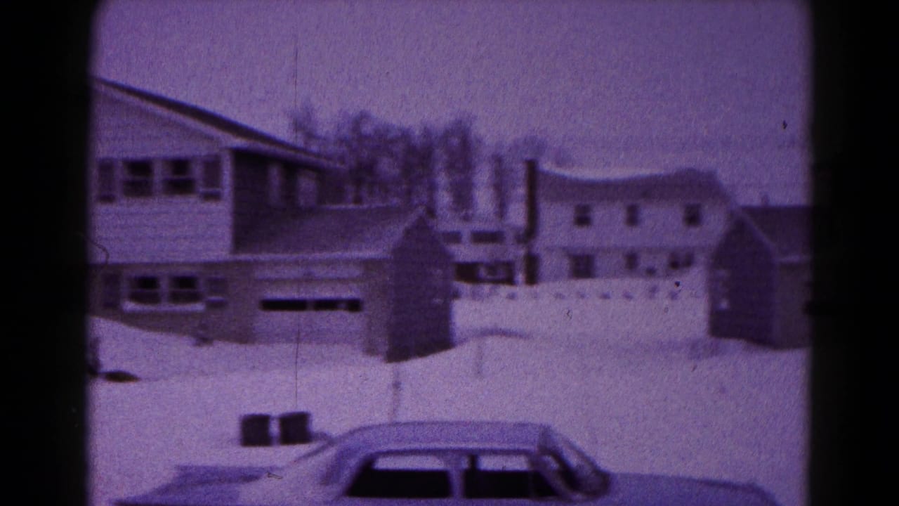 1959 Hagerstown home-movie frame showing snow-covered houses, garages, fences, and a car partly buried in snow.