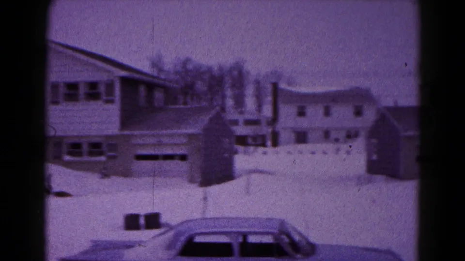 1959 Hagerstown home-movie frame showing snow-covered houses, garages, fences, and a car partly buried in snow.