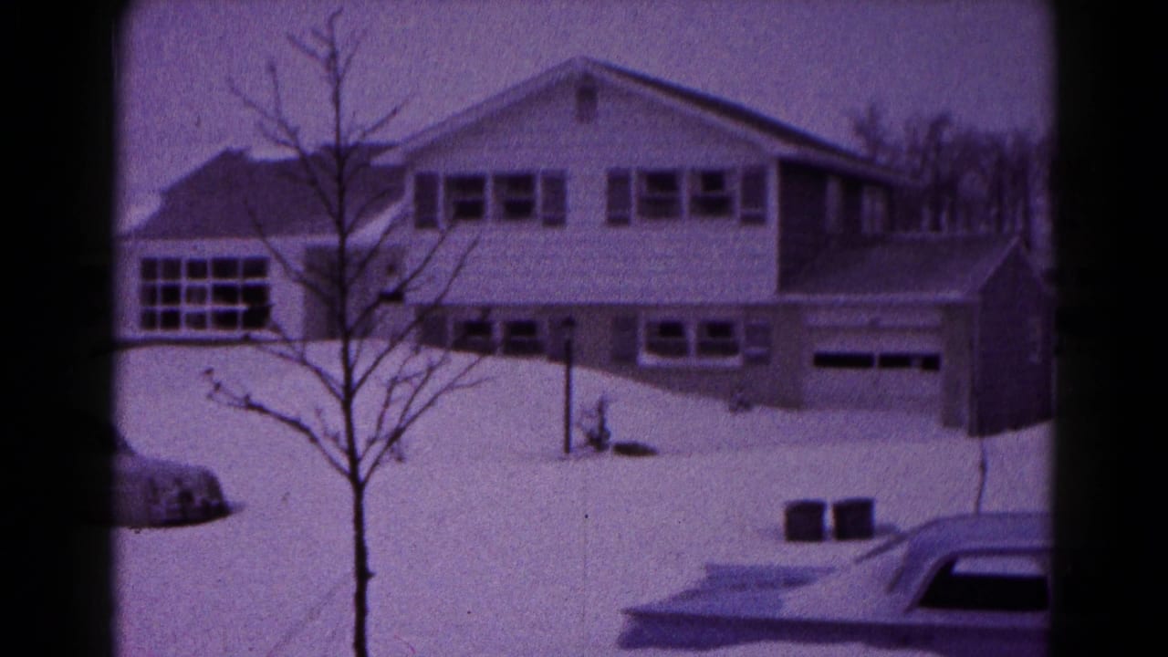 Snowbound 1959 Hagerstown residential view with a two-story house, garage doors, bare tree, and parked car edge.