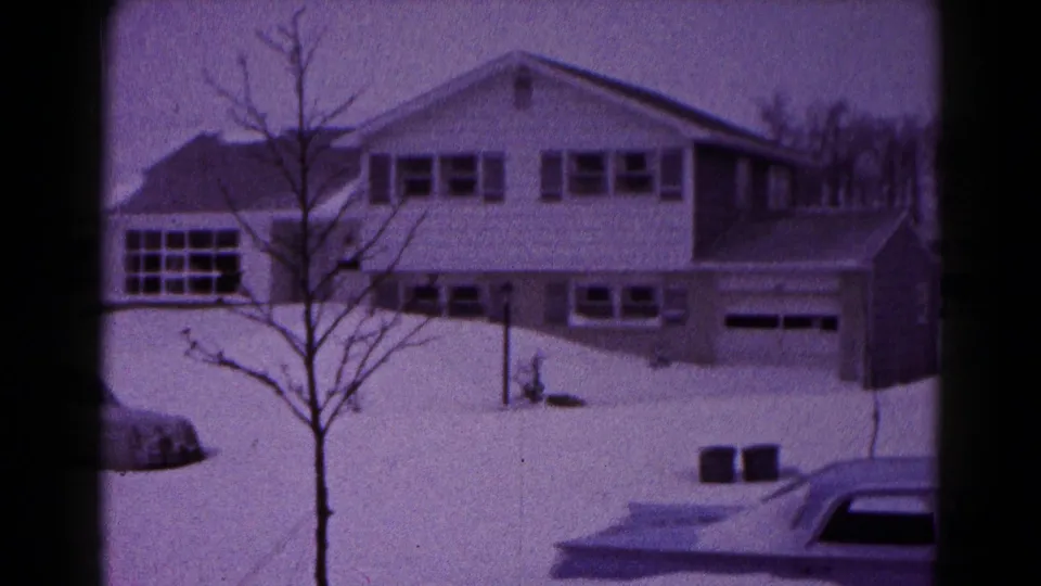 Snowbound 1959 Hagerstown residential view with a two-story house, garage doors, bare tree, and parked car edge.