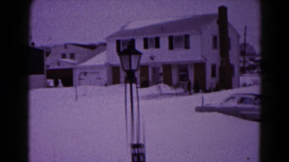 1959 Hagerstown residential snow scene showing two-story houses, a lamppost, chimney, snowbanks, and a car partly buried at frame edge.