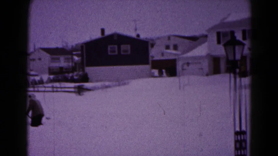 1959 Hagerstown home-movie frame showing deep snow across residential yards, houses, fencing, and a distant person near the left edge.