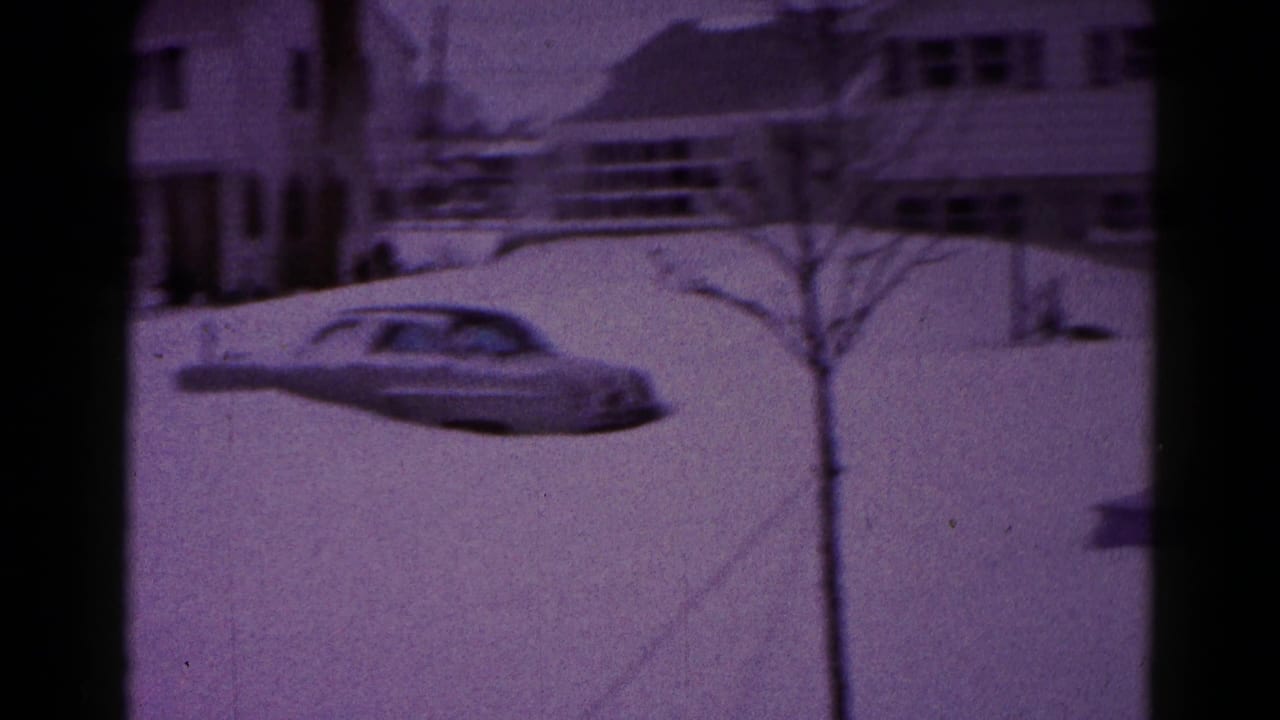 1959 Hagerstown-area home-movie frame showing a sedan partly buried in deep snow outside detached houses.