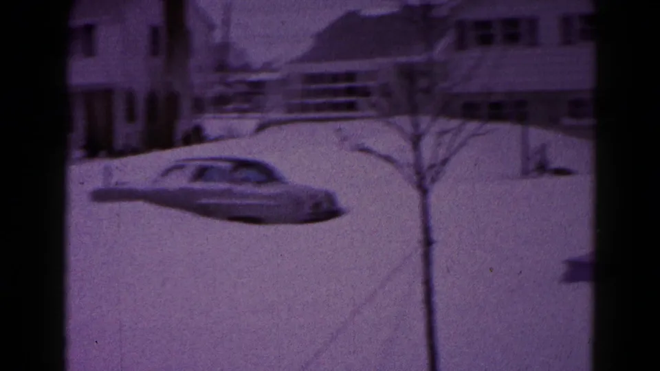 1959 Hagerstown-area home-movie frame showing a sedan partly buried in deep snow outside detached houses.