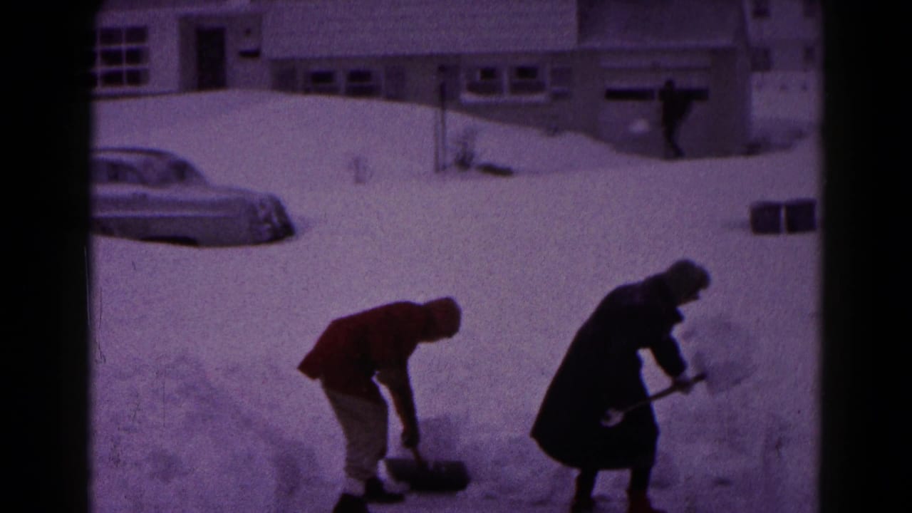 In 1959 Hagerstown, Maryland, two bundled people shovel snow in a residential yard with a snow-covered car and houses behind them.