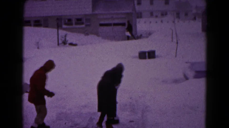 Two people in winter coats move through deep snow in a Hagerstown residential setting, with houses and snowbanks visible behind them.