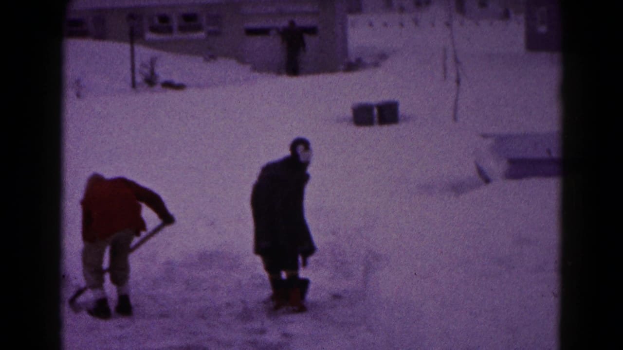 Two men continue clearing snow near houses and snowbanks.