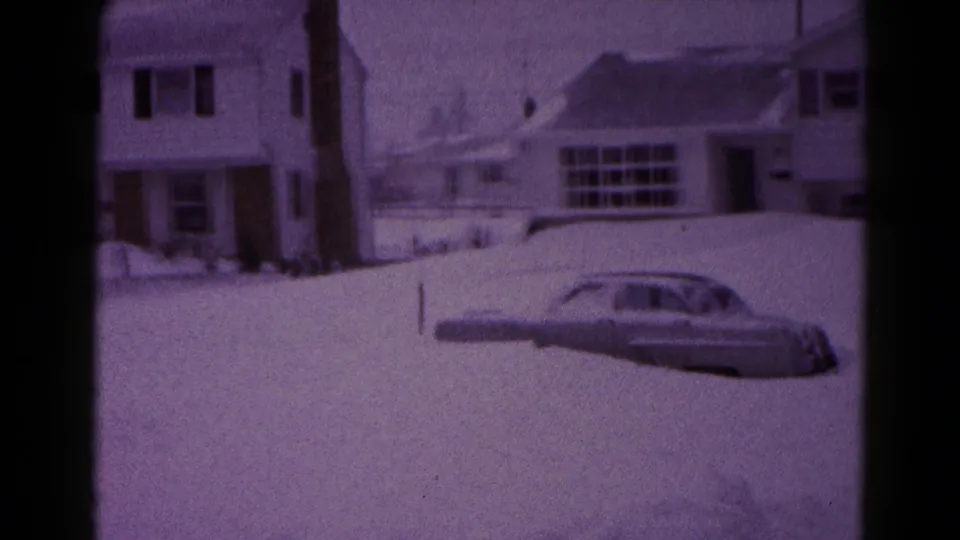 1959 Hagerstown winter frame with a grey mid-century car surrounded by snowbanks in front of suburban homes.