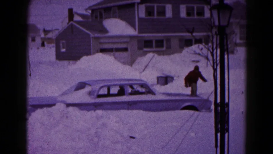 In Hagerstown, Maryland, 1959, a man approaches a snow-buried four-door sedan on a residential street.