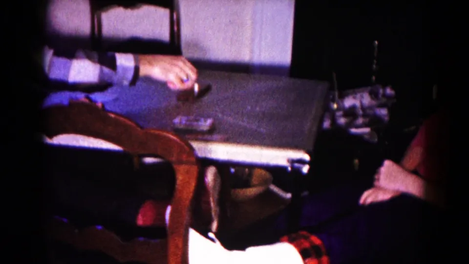 The card table fills the frame as an adult's hand reaches across it, with the seated woman partly visible nearby.