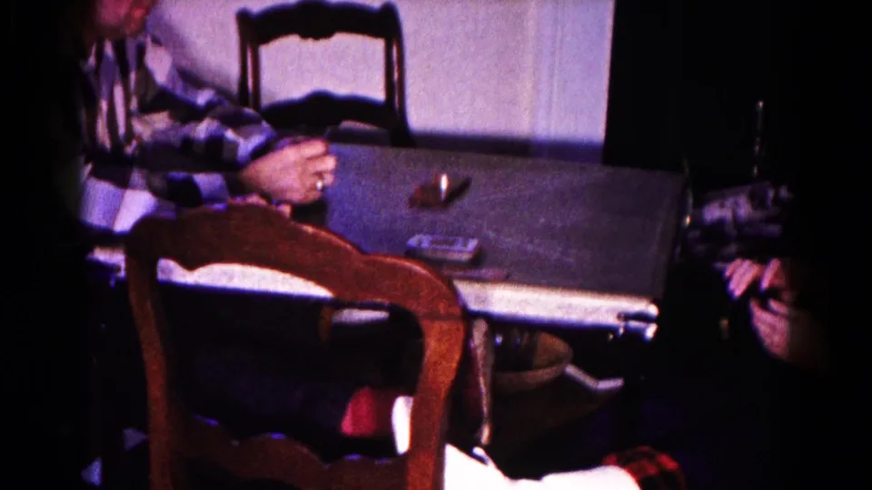 The card table, chairs, and scattered playing cards remain visible as the man sits partly out of frame in the home interior.