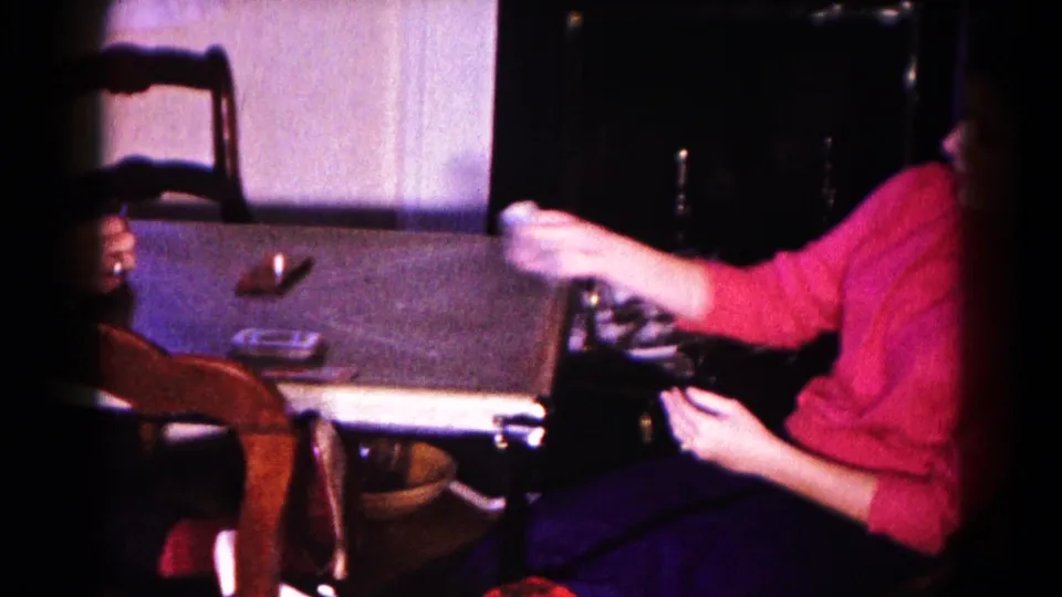 A woman in a bright pink sweater reaches across the table while cards are in play in the 1959 Hagerstown home movie.