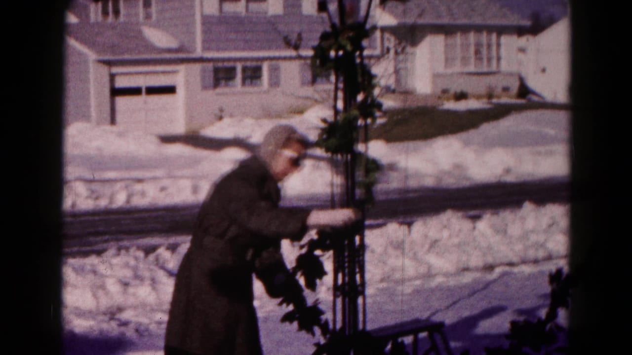 In Hagerstown, Maryland in 1959, an adult in winter clothing adjusts garland outside a house beside a snow-covered street.