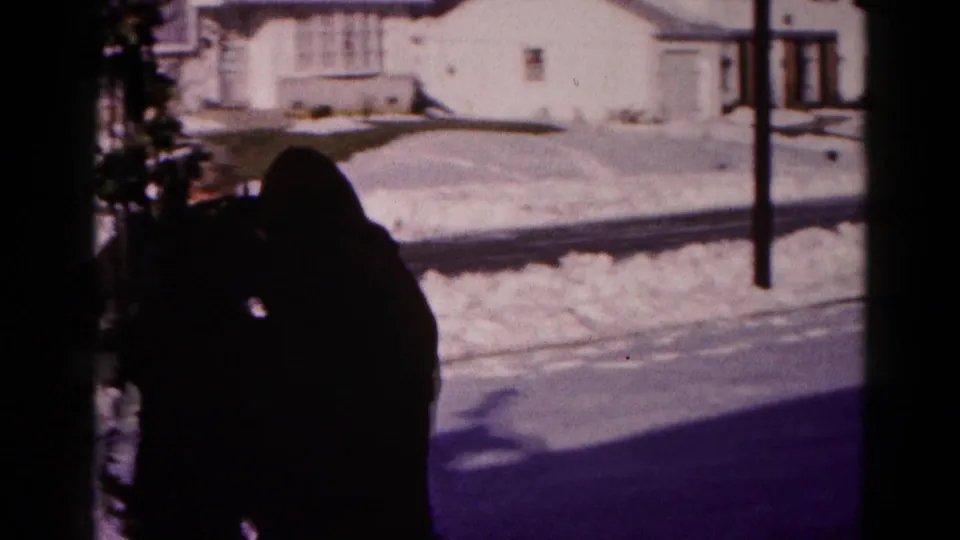 A silhouetted adult adjusts outdoor garland in a snowy Hagerstown neighborhood, with houses and a street visible beyond.