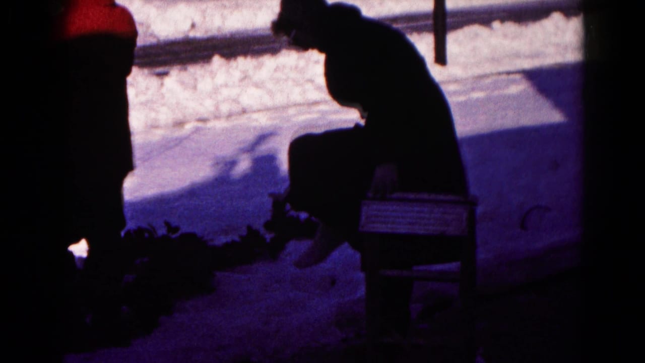 Dark silhouette of a seated man bending over on a bench beside snow.