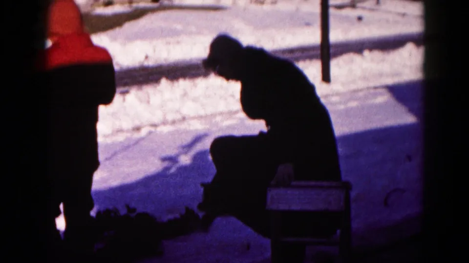 The 8mm frame shows the man seated in a snowy residential yard in Hagerstown, bent over as a red-hooded figure stands nearby.