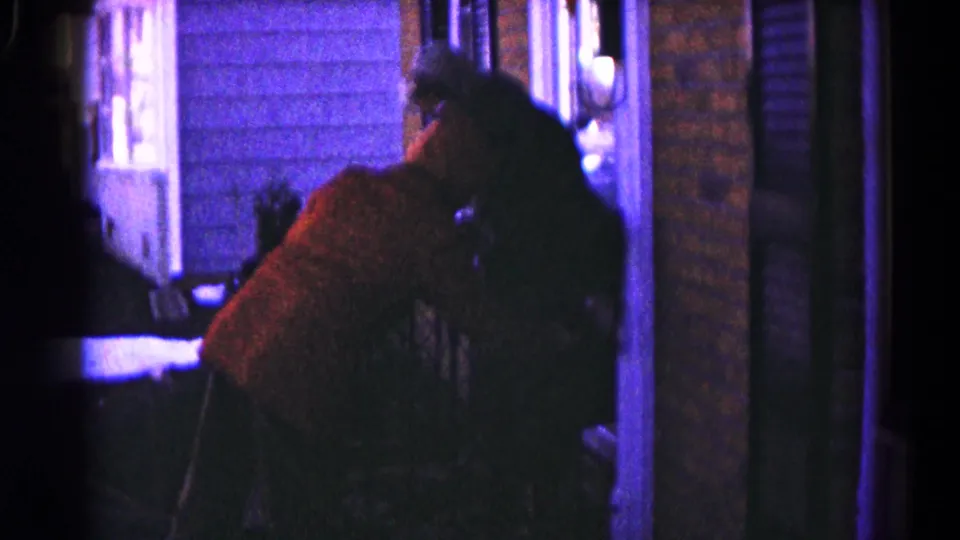 Two people sit close together near a porch doorway and wall lamp in low-light 1959 Hagerstown 8mm footage.