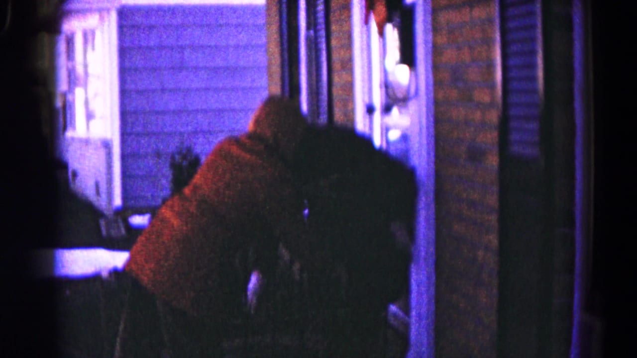 Person in a red sweater bends near a doorway in dim indoor light.
