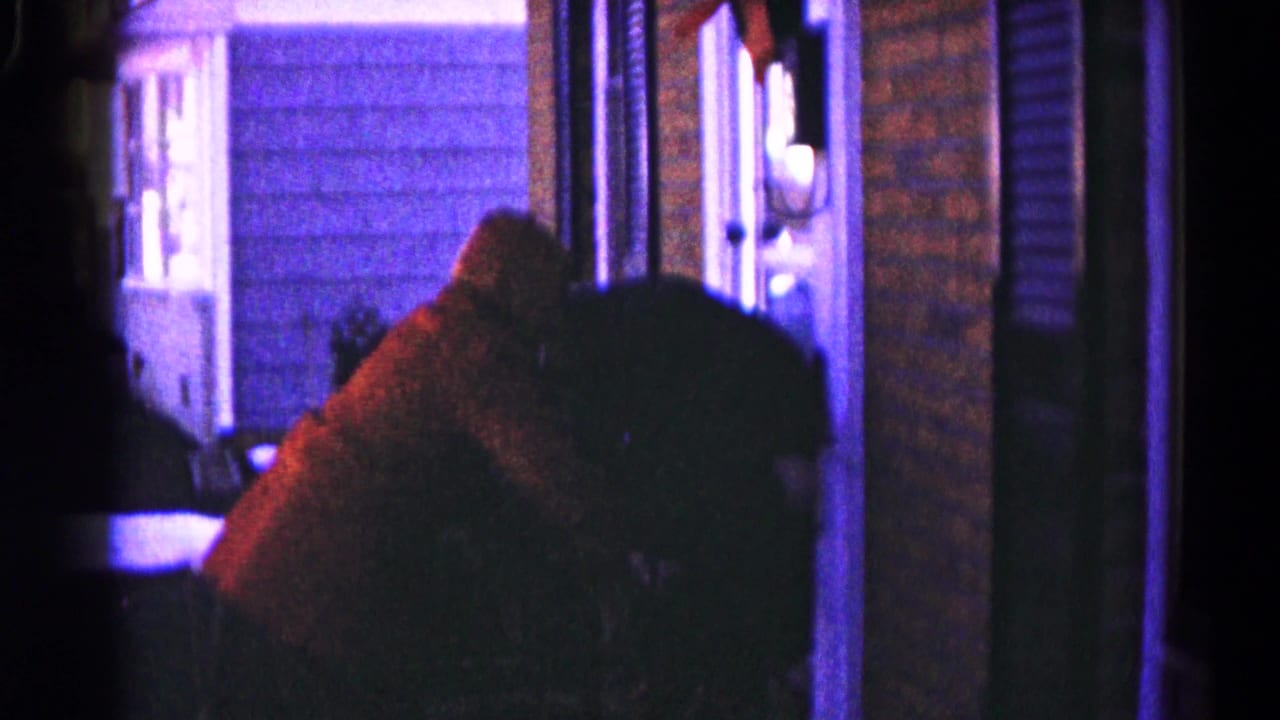 A person in a red sweater leans in a shadowed doorway area.