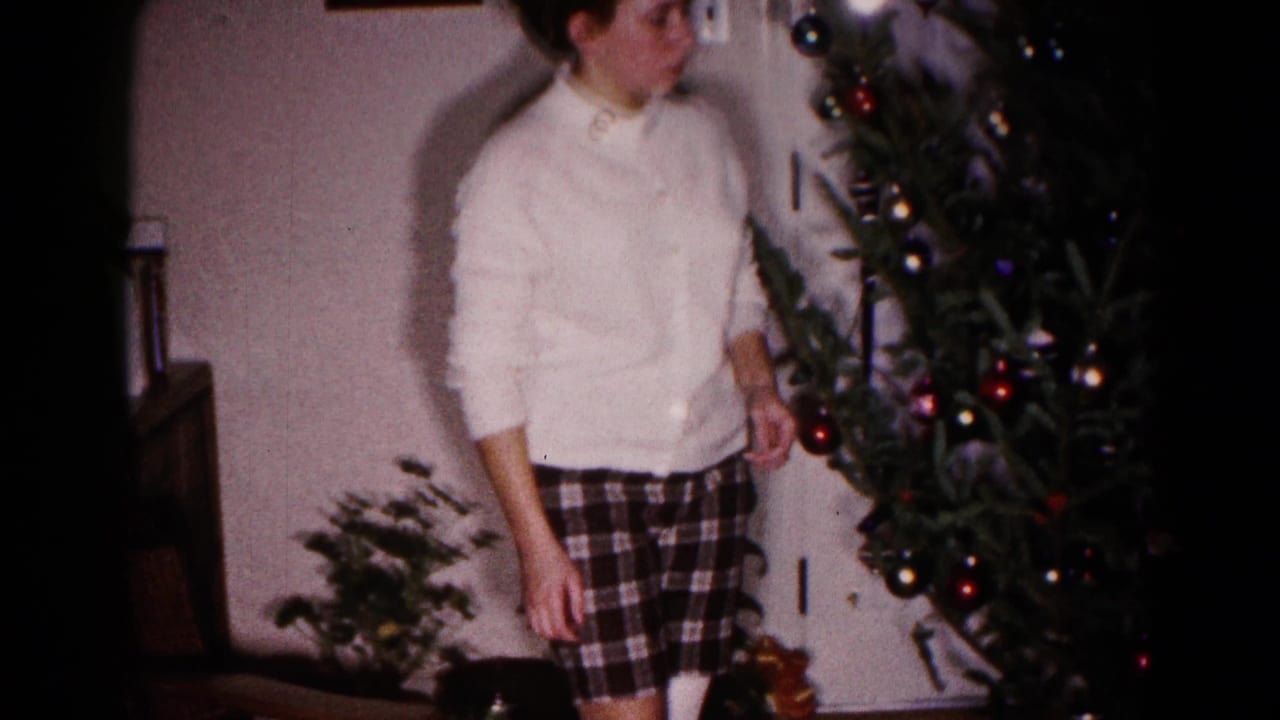Young woman stands near a Christmas tree with ornaments in a home interior.