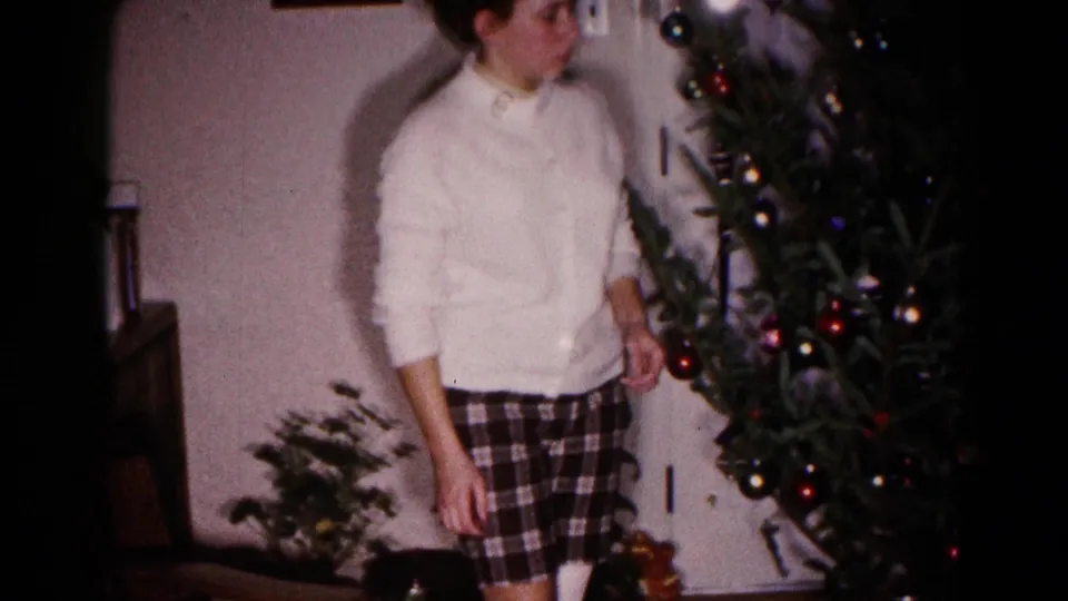 The young woman stands beside the ornamented Christmas tree in the Hagerstown living room, with wall trim and plants visible nearby.