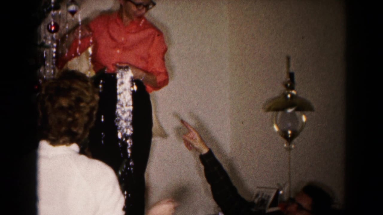 Woman in a red shirt reaches toward a Christmas tree while others point from below.