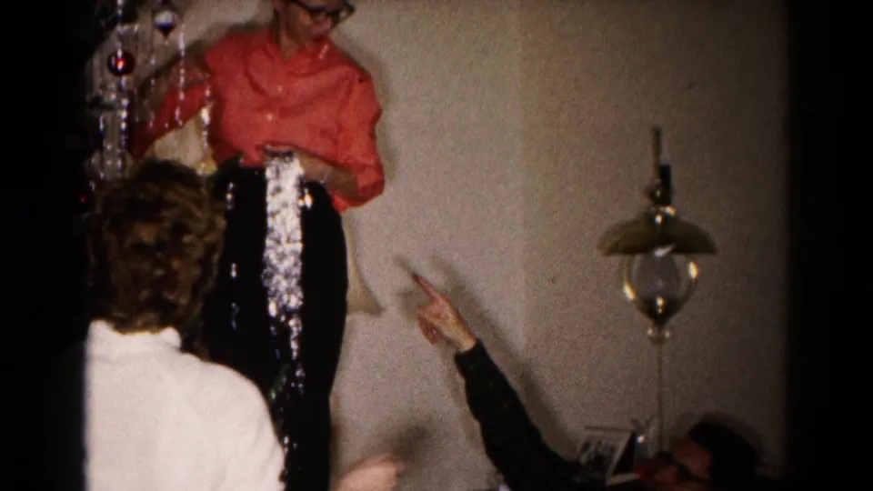 1959 Hagerstown home-movie frame showing adults helping a woman place silver tinsel on an indoor Christmas tree.