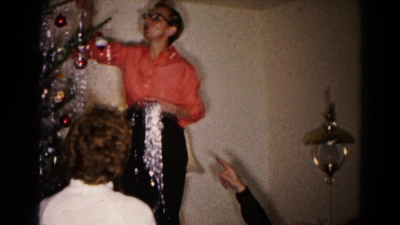 Woman on a stool adjusts tinsel near the top of a Christmas tree as others gesture.