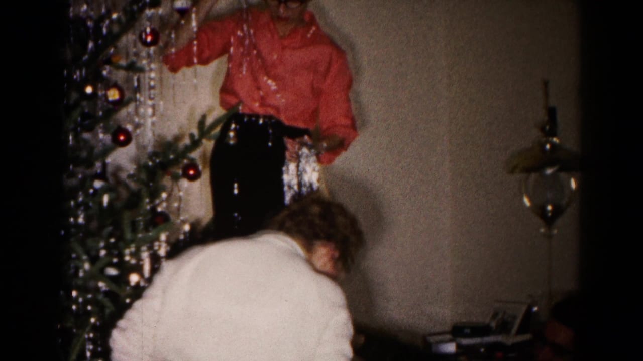 A woman stands by a decorated Christmas tree while another bends forward below.