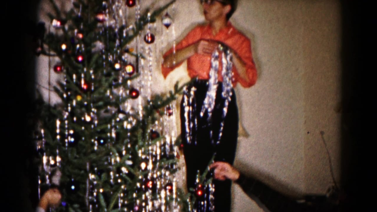 Man beside a Christmas tree holds silver tinsel while ornaments hang from the branches.