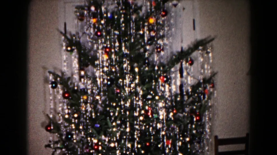 1959 Hagerstown home-movie view of a tinsel-covered Christmas tree beside a wooden chair in a private interior.