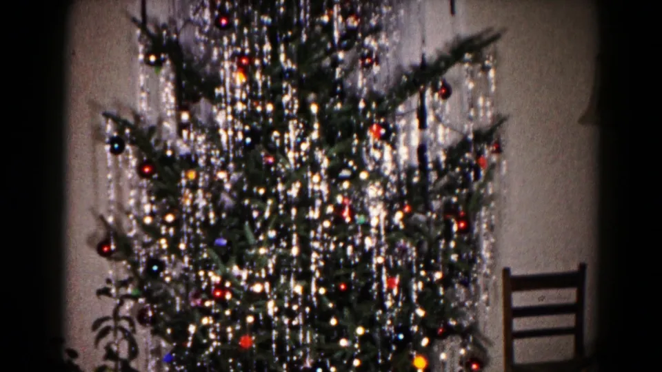 1959 Hagerstown home-movie frame showing the lower portion of a decorated Christmas tree with ornaments, tinsel and nearby household furniture.