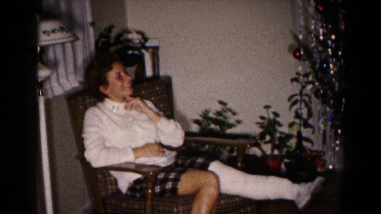 Woman in a white sweater sits in an armchair with one leg in a cast near a Christmas tree.