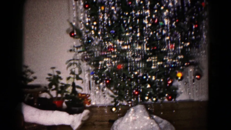 1959 Hagerstown home-movie frame showing a decorated Christmas tree with silver tinsel, ornaments, plants, and a table edge.