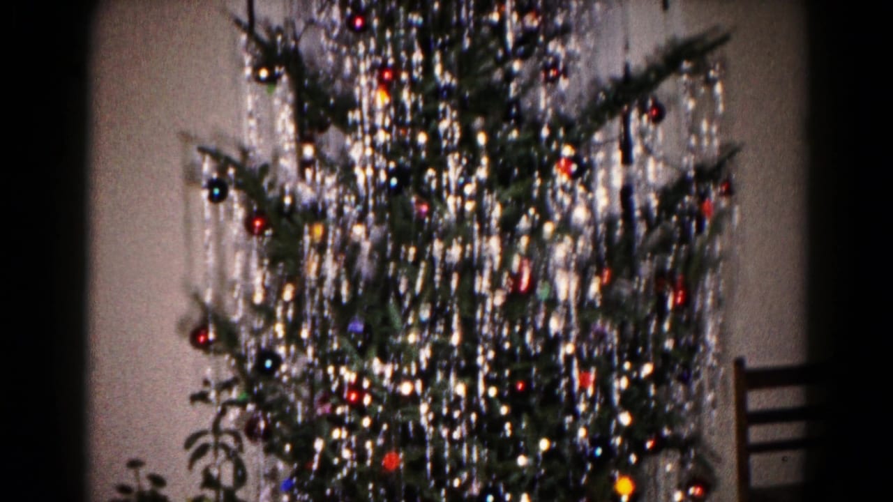 1959 Hagerstown home-movie frame centered on a tinsel-covered Christmas tree with ornaments and a chair at the right edge.