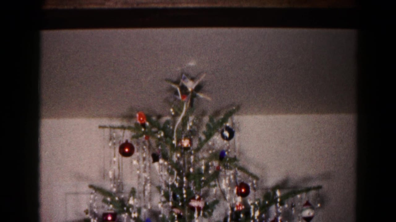 Decorated Christmas tree top with star, ornaments, and silver tinsel against an indoor wall.