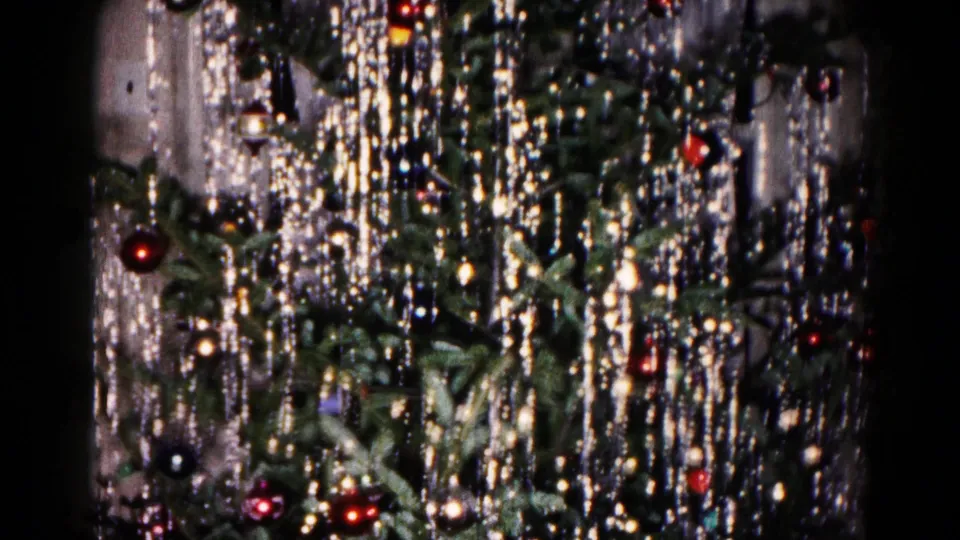 1959 8mm holiday frame showing the lower decorated tree, with dense tinsel, red glass ornaments, dark baubles, and evergreen branches.