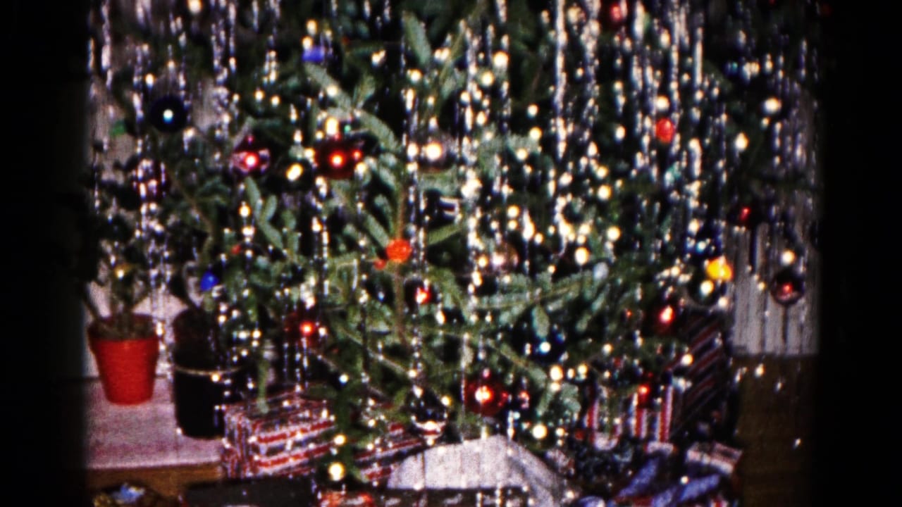 The camera pulls back on the decorated Christmas tree, revealing wrapped presents and nearby potted plants in a 1959 home interior.
