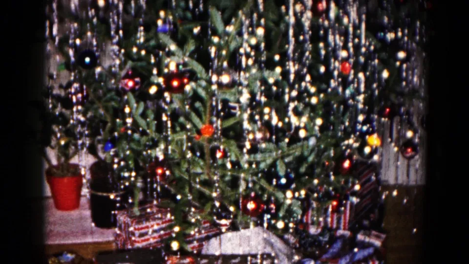 The camera pulls back on the decorated Christmas tree, revealing wrapped presents and nearby potted plants in a 1959 home interior.