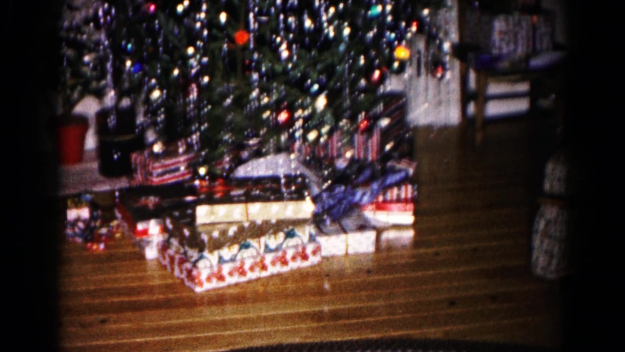 1959 Hagerstown home-movie frame showing a lit Christmas tree, tinsel, and wrapped presents on a wood floor.