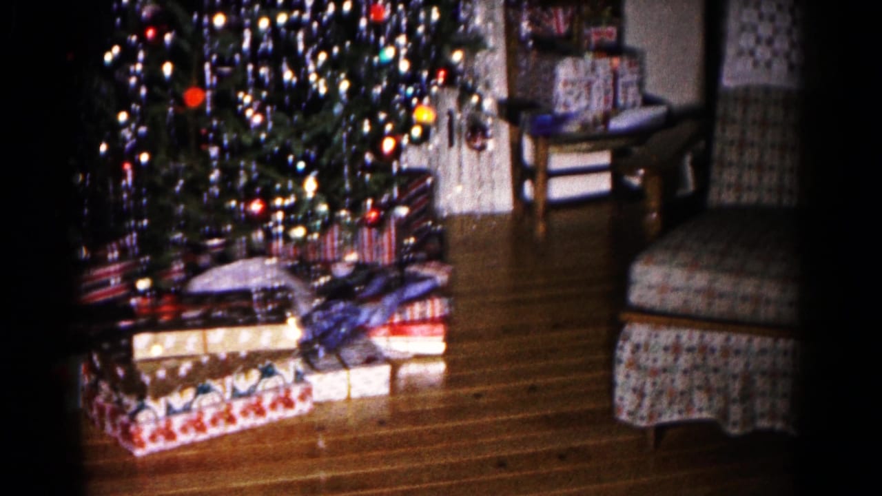 Wrapped presents beneath a decorated Christmas tree beside a patterned chair.