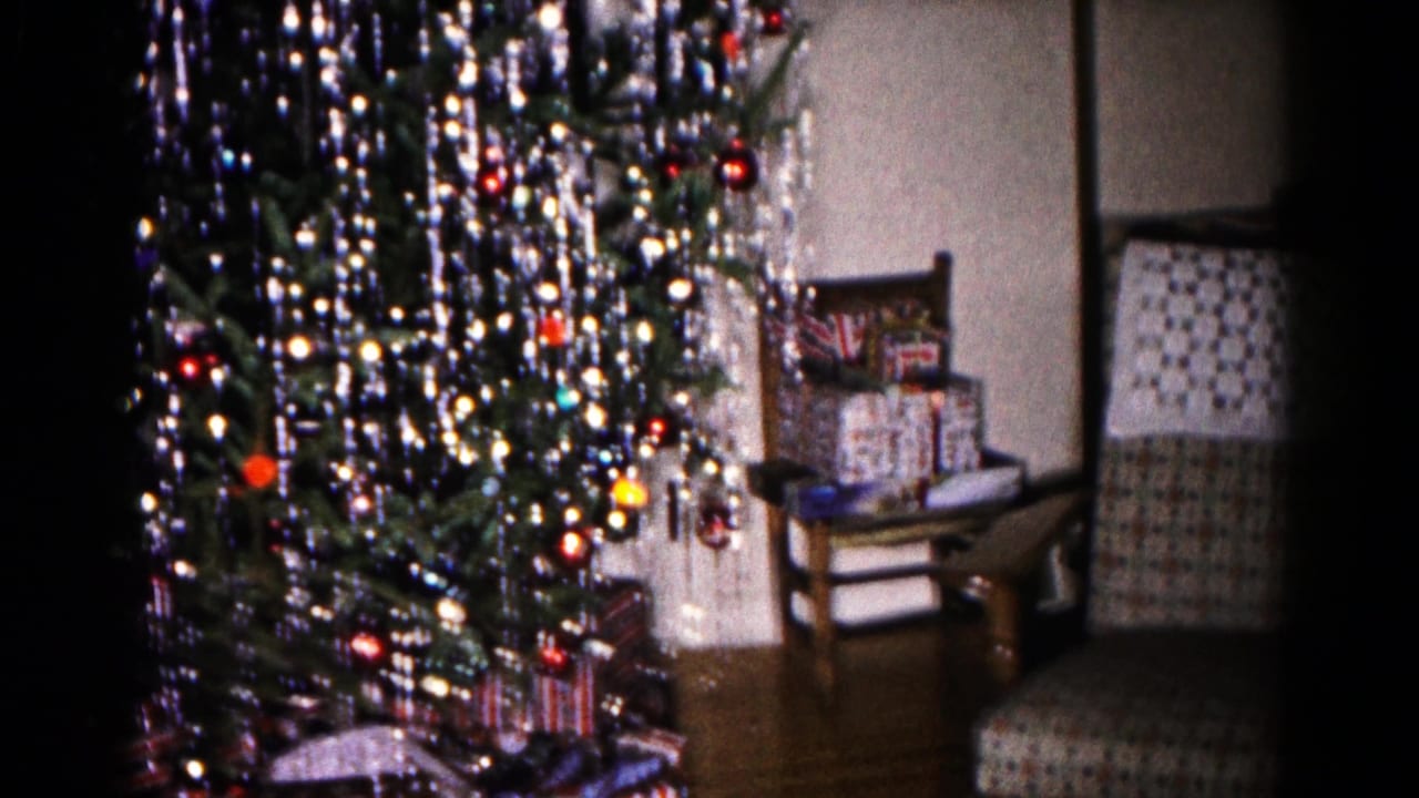 1959 Hagerstown home-movie frame showing a tinsel-covered Christmas tree, wrapped gifts, ornaments, and nearby upholstered chairs.