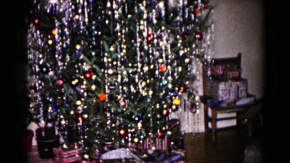 1959 Hagerstown frame with a decorated Christmas tree, dense silver tinsel, colored ornaments, wrapped presents, and a chair at right.