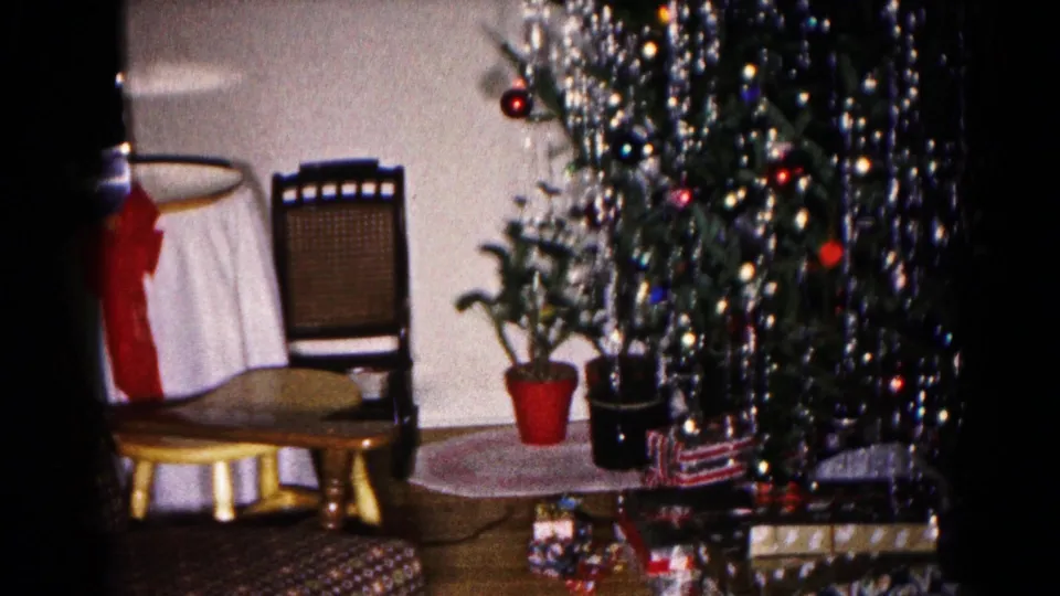1959 Hagerstown frame showing a decorated Christmas tree beside potted plants, a round table, a wooden chair, and wrapped gifts.