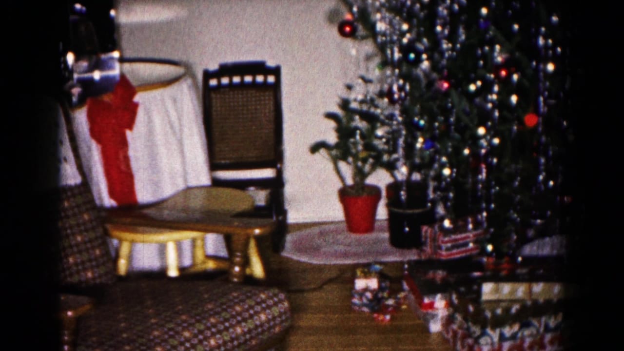 1959 Hagerstown home-movie frame showing a decorated Christmas tree, patterned seating, wrapped gifts, and a white table covering with a large red bow.